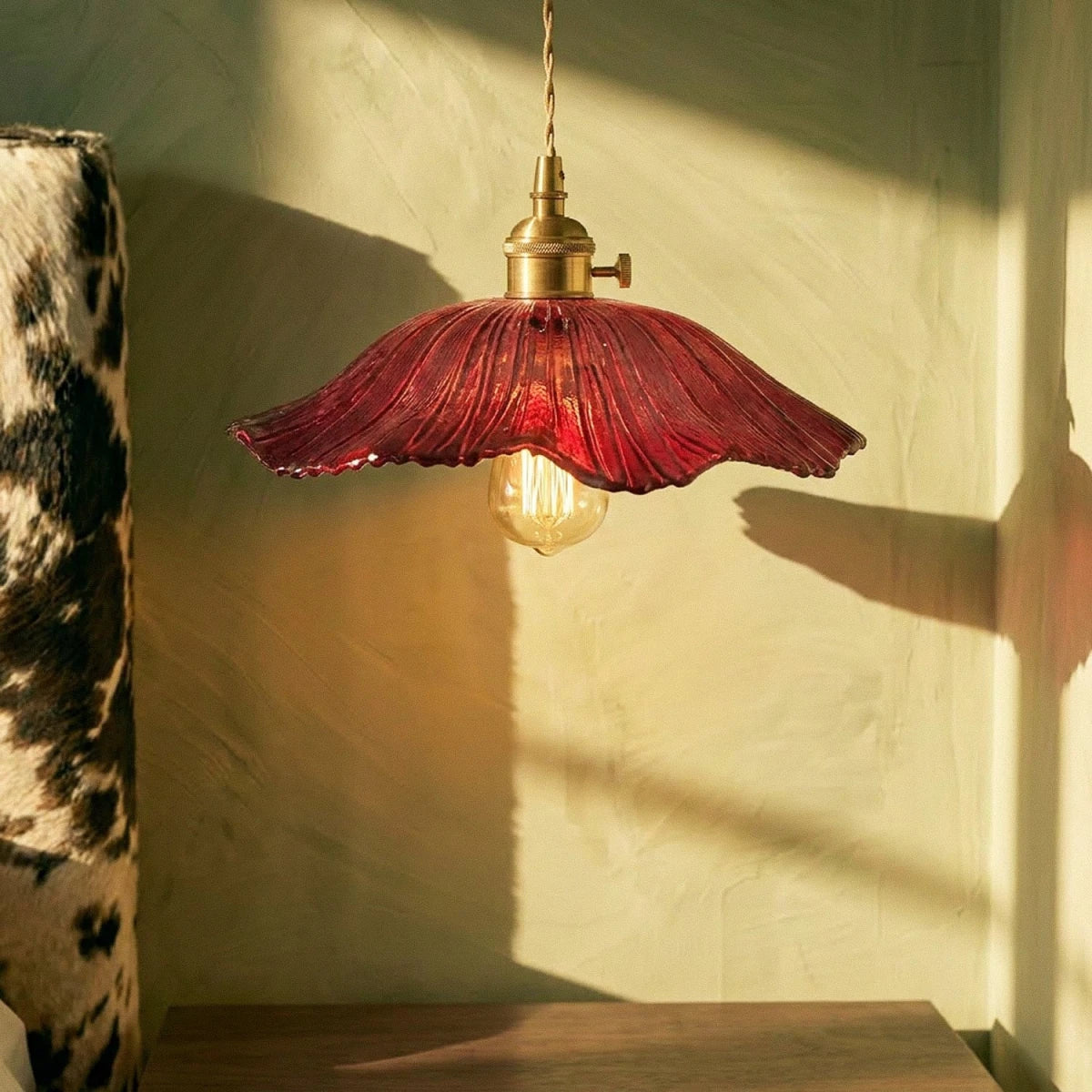 Clérachic red ribbed glass pendant with a brass switch holder and an amber filament bulb, close up against a sunlit plaster wall.