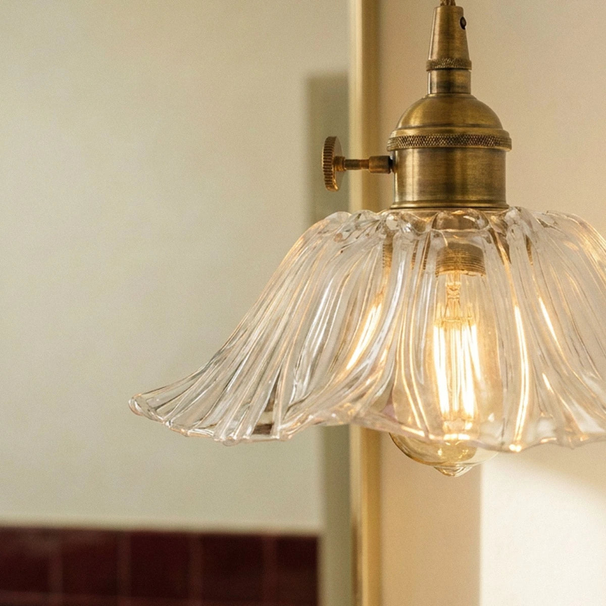 Clérachic clear ribbed glass shade with a rippled edge and an aged brass cap and switch, lit by a warm filament bulb up close.