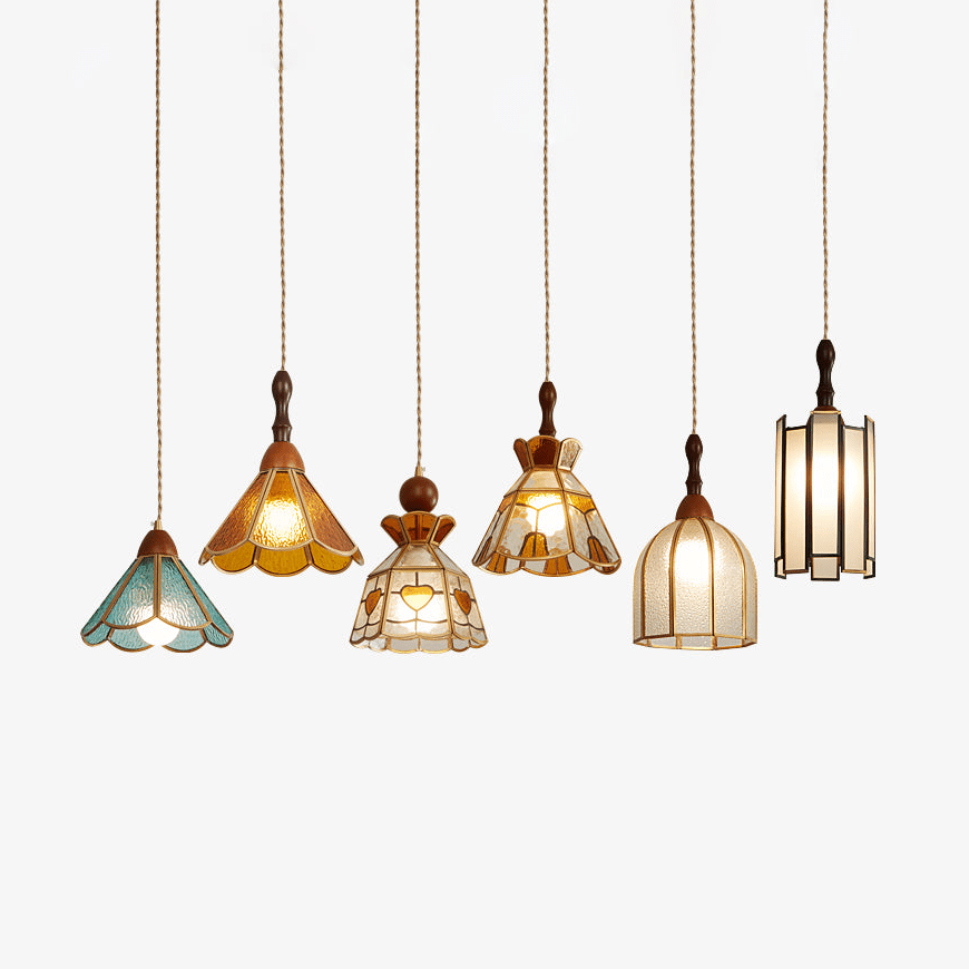 Six shapes of this Clérachic stained glass pendant in a row, in amber, teal, clear and frosted glass with brass trim, on a white backdrop.