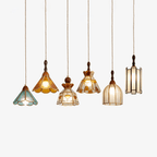 Six shapes of this Clérachic stained glass pendant in a row, in amber, teal, clear and frosted glass with brass trim, on a white backdrop.