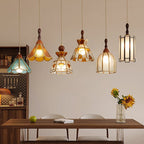 Six Clérachic stained glass pendants at staggered heights above a walnut dining table, with a vase of sunflowers and a pegboard shelf behind.