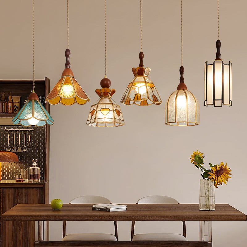 Six Clérachic stained glass pendants at staggered heights above a walnut dining table, with a vase of sunflowers and a pegboard shelf behind.