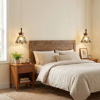 Two Clérachic stained glass pendants with heart-shaped amber panels hanging either side of a wooden bed in a warm cream bedroom.