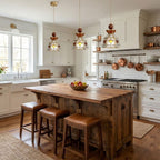 Three Clérachic heart-panel stained glass pendants over a rustic wooden kitchen island with leather stools and copper pans behind.