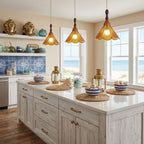 Three amber Clérachic pendants with scalloped shades over a pale kitchen island, with seaside windows and blue patterned tiles behind.