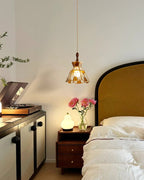 A Clérachic heart-panel pendant lit beside a bed with a mustard headboard, a bedside table with pink flowers and a record player.