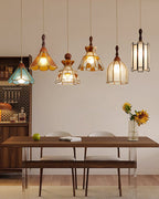 Six Clérachic pendants, shown as a set, hanging in a staggered line over a walnut table with a sunflower vase and a bookshelf.