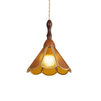 Amber Clérachic pendant with a flared scalloped shade of textured glass, a wooden finial and a twisted cord, lit on white.