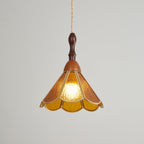 Amber Clérachic pendant on a grey backdrop, its textured glass petals edged in brass and lit from within by a warm bulb.