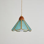 Teal Clérachic pendant on grey with a wooden cap, textured glass panels in brass edging and the bulb just visible beneath.