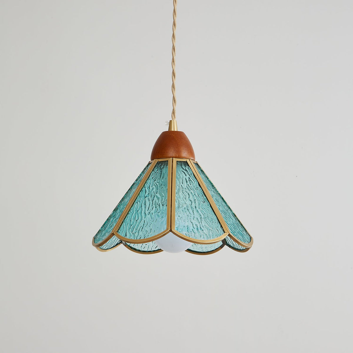 Teal Clérachic pendant on grey with a wooden cap, textured glass panels in brass edging and the bulb just visible beneath.