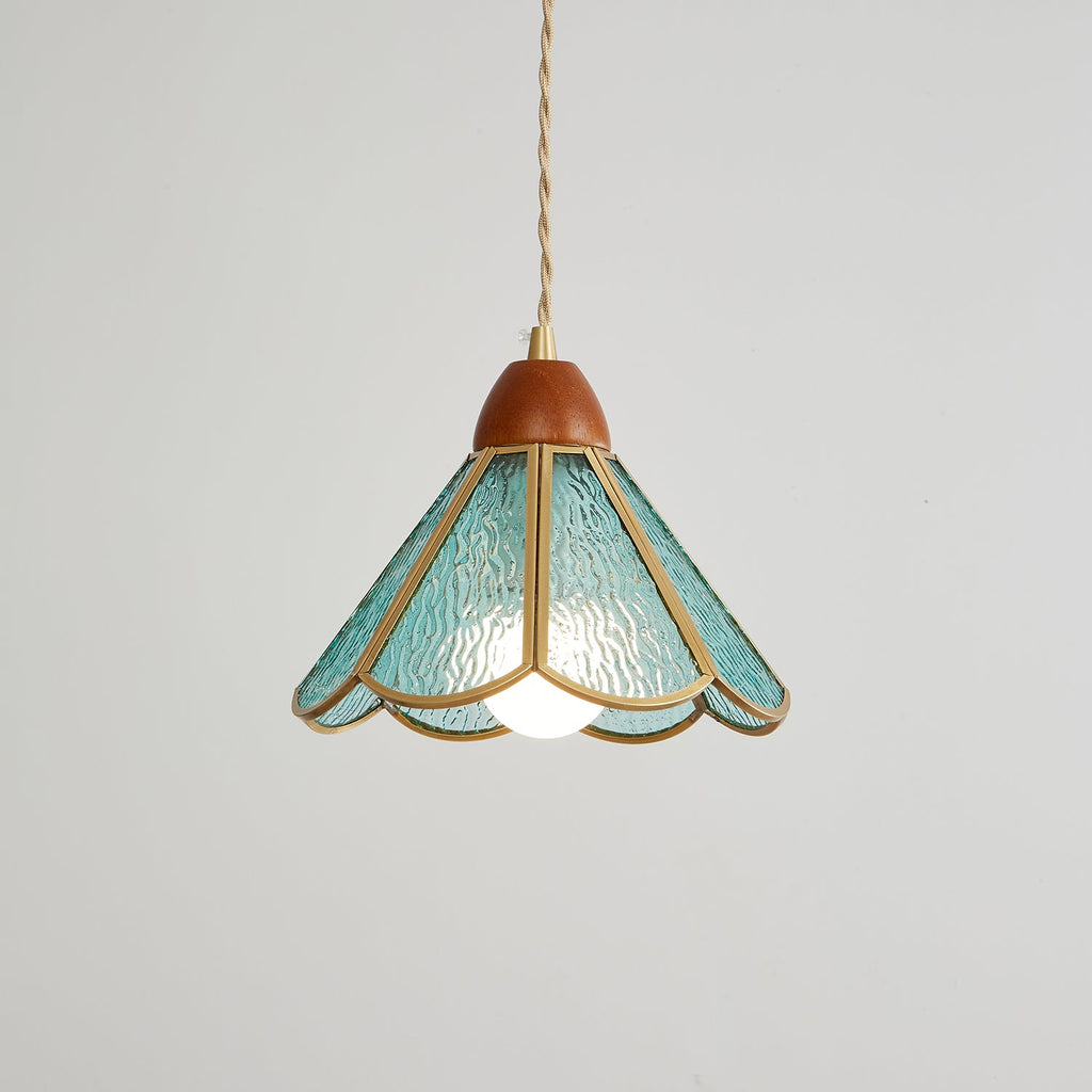 Lit teal Clérachic pendant on a grey backdrop, a bulb glowing under a scalloped shade of rippled glass with brass edging.