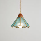 Lit teal Clérachic pendant on a grey backdrop, a bulb glowing under a scalloped shade of rippled glass with brass edging.