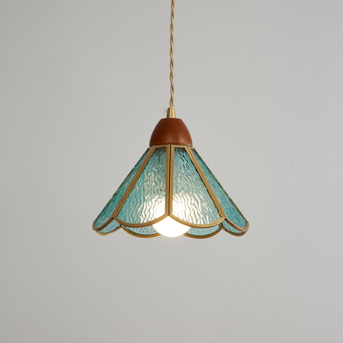 Teal Clérachic pendant lit on a mid-grey backdrop, its rippled glass petals lit from within and its wooden cap above.
