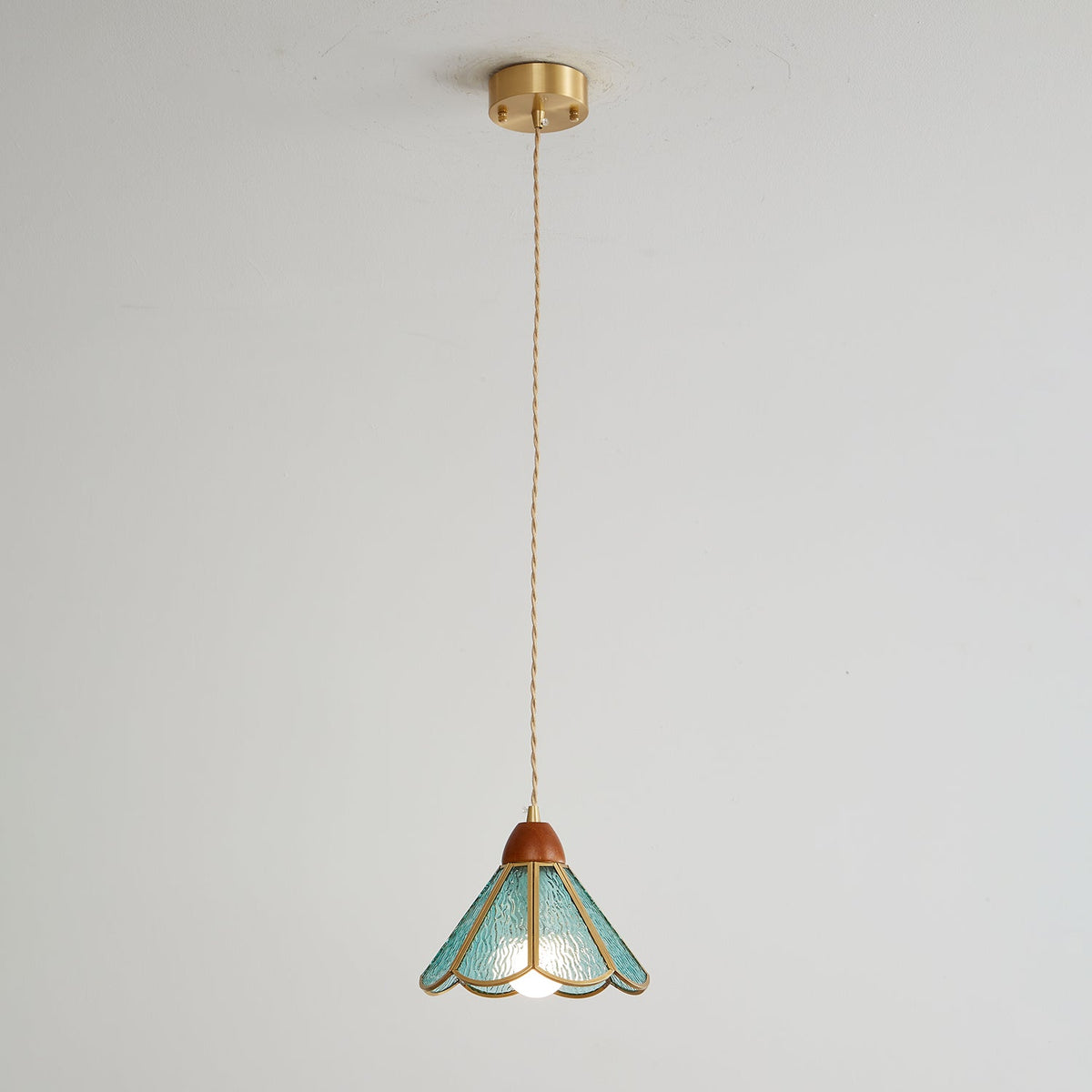 Small teal Clérachic pendant on a long twisted cord from a brass ceiling canopy, shown on a pale grey wall.