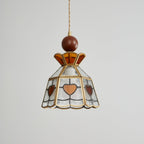 Unlit Clérachic heart-panel pendant on grey, with a wooden ball finial, an amber crown and clear textured glass in brass.