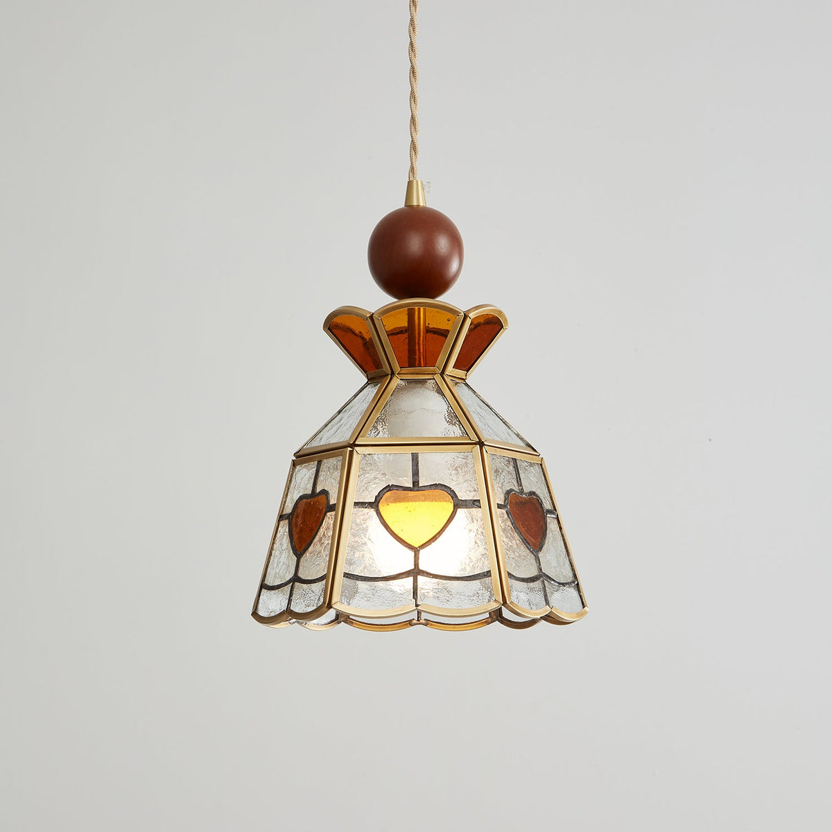 Lit Clérachic heart-panel pendant on grey, the amber hearts glowing at the front of its clear glass shade.