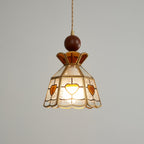 Closer view of the lit Clérachic heart-panel pendant, its amber crown and brass ribs sharp against a pale grey wall.