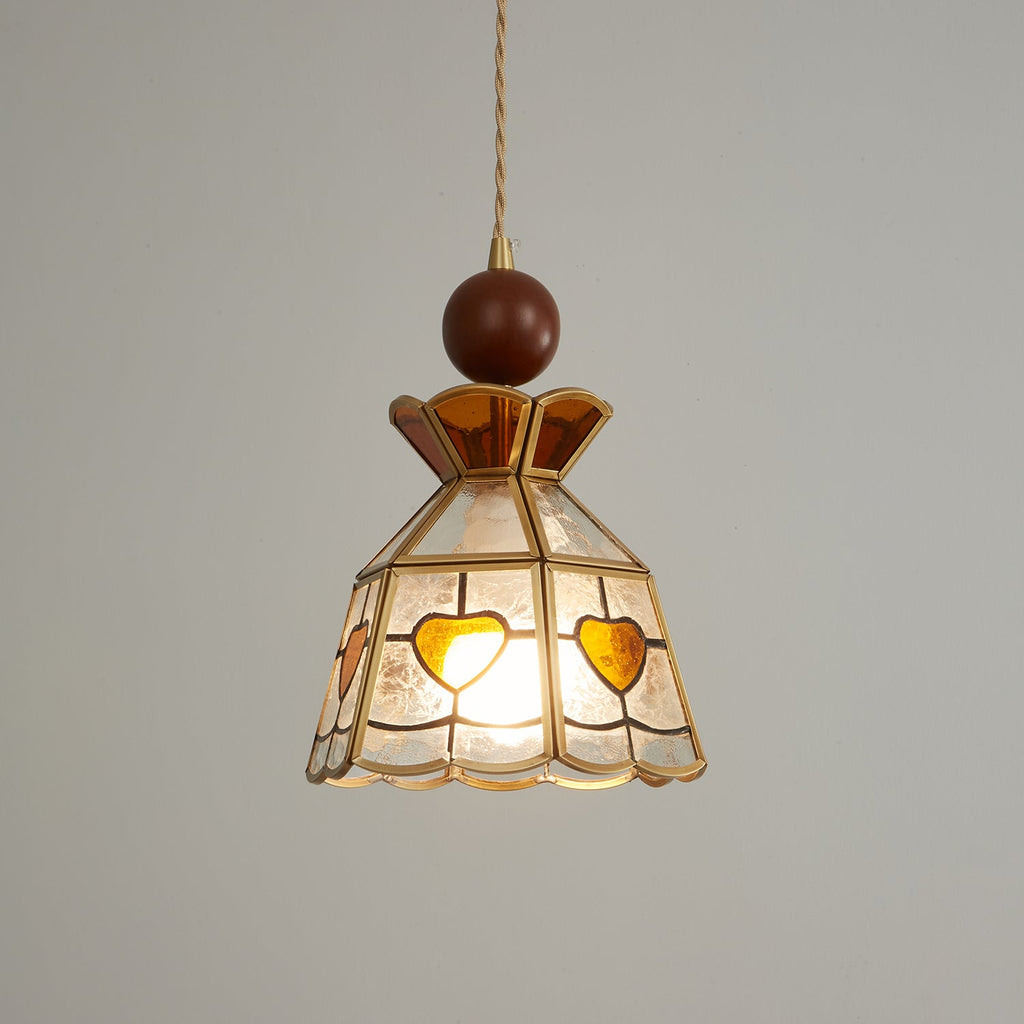 Warm-lit Clérachic stained glass pendant with amber hearts, its textured clear glass glowing against a soft grey wall.