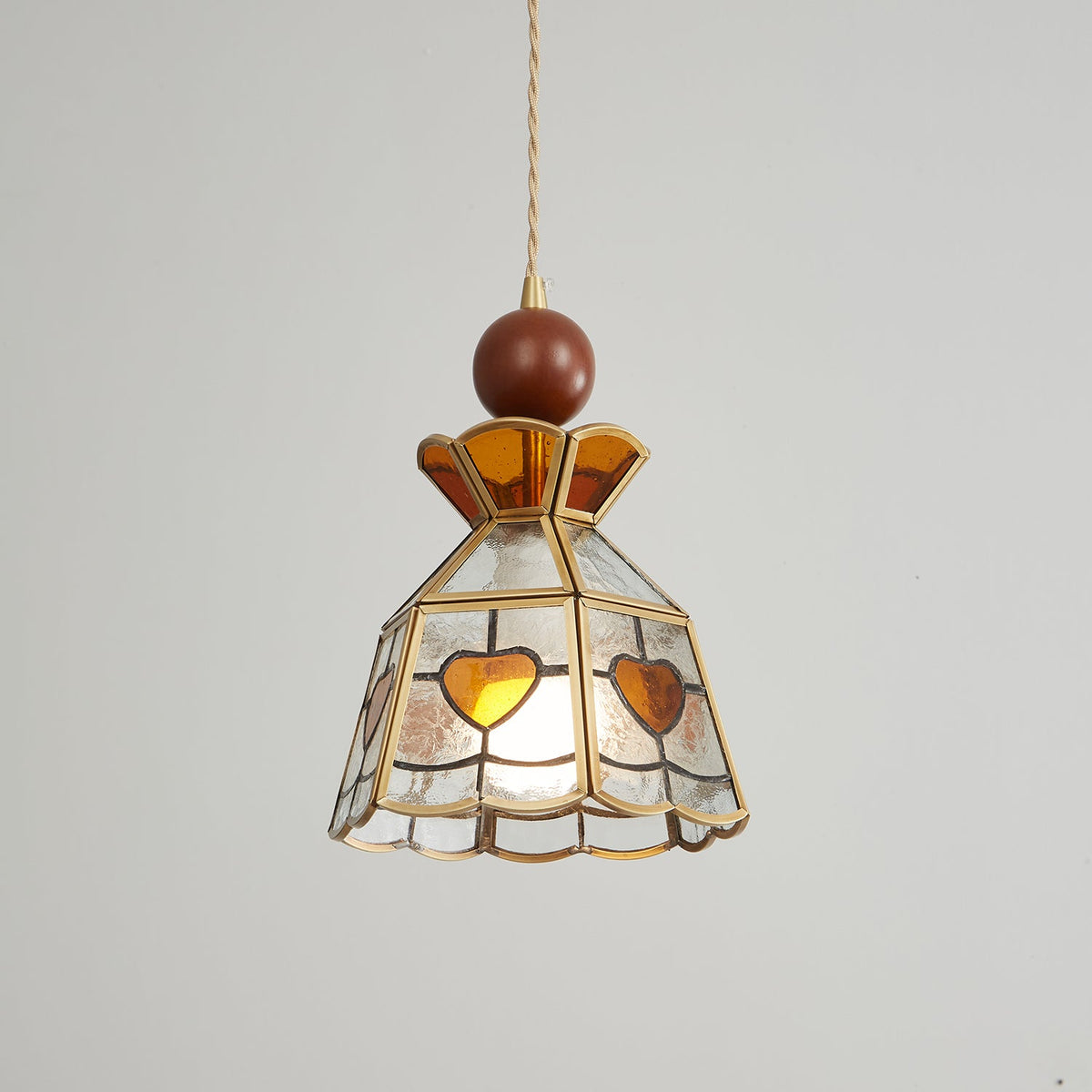 Dimly lit Clérachic heart-panel pendant on a pale backdrop, the amber hearts and brass ribs clearly visible.