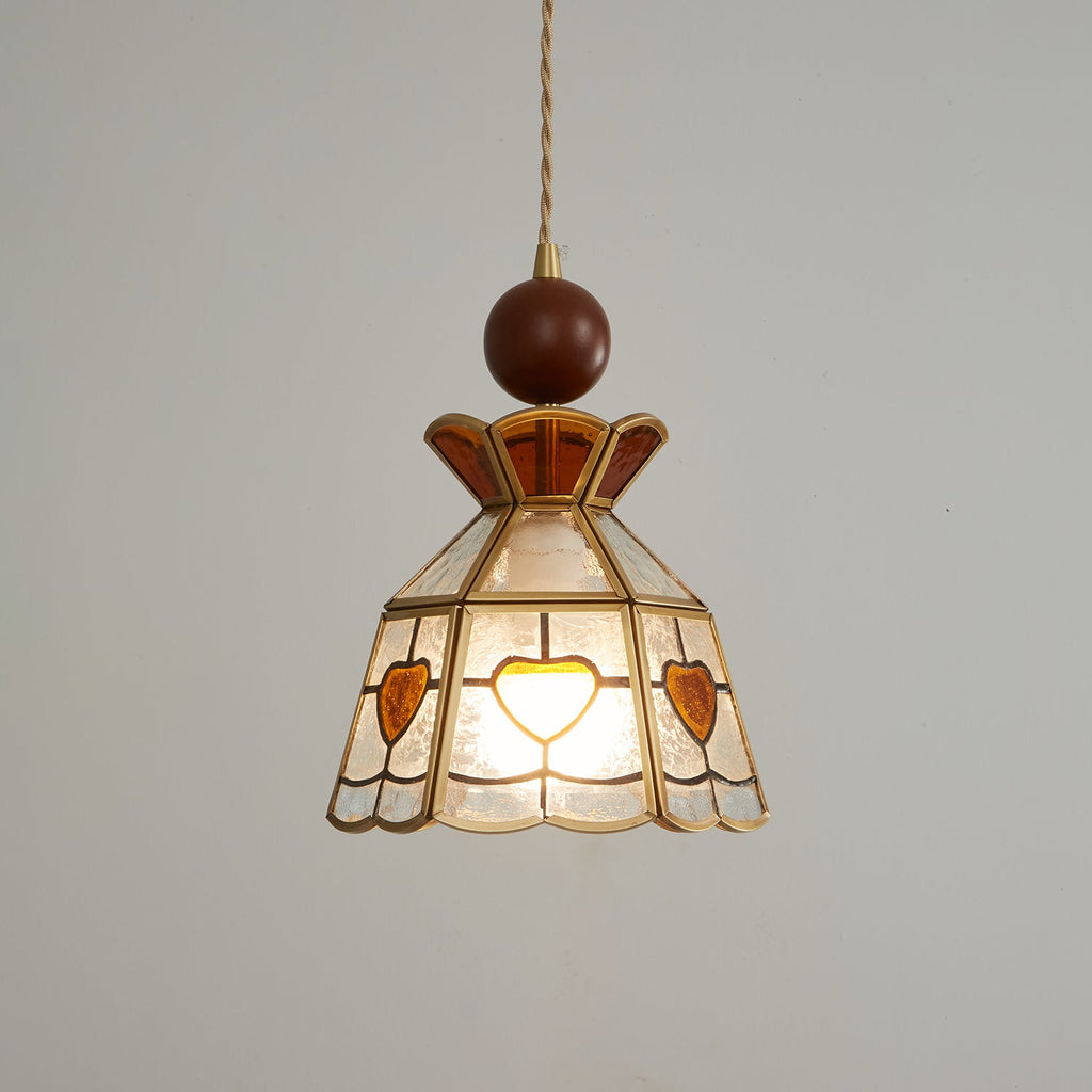 Clérachic heart-panel pendant, lit, with its wooden ball and brass fitting at the top, photographed on a grey backdrop.