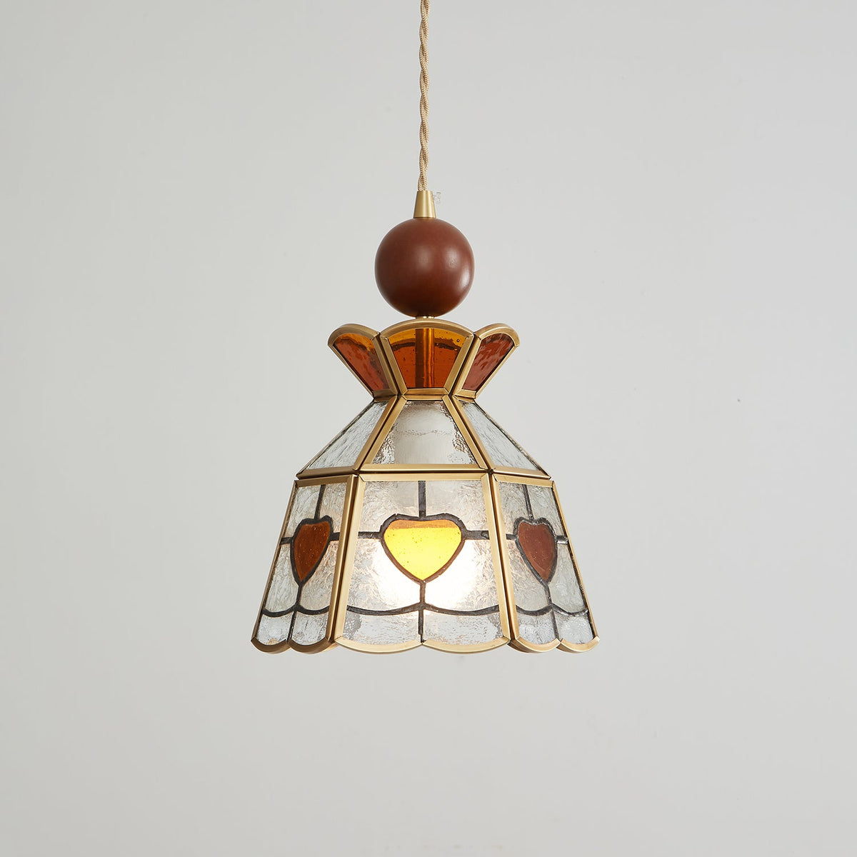 Clérachic heart-panel pendant switched off, showing its pale textured glass, amber hearts and brass frame on grey.