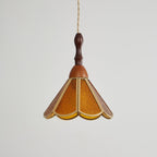 Unlit amber Clérachic pendant with a flared scalloped shade of textured glass and a turned wooden finial, on pale grey.