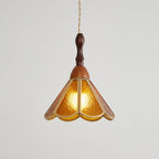 Side view of the amber Clérachic pendant, lit, the rippled glass glowing yellow-orange inside its brass-edged petals.