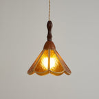 Amber Clérachic pendant lit on a grey backdrop, a warm glow through the petal-shaped glass panels and a wooden cap above.