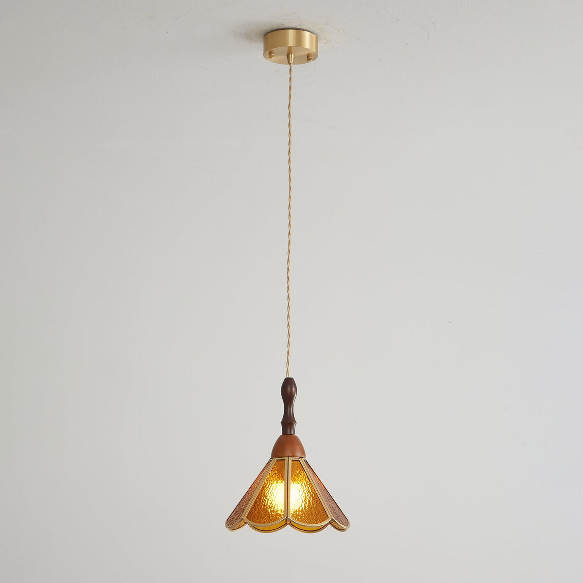 Amber Clérachic pendant on a long cord from a brass canopy, small against a pale grey wall.