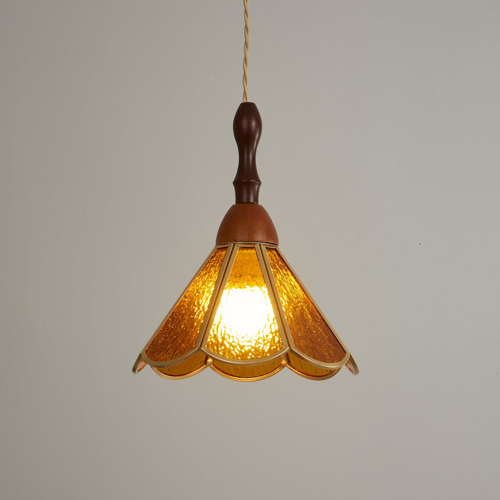 Closer view of the lit amber Clérachic pendant, its deep gold glass petals bright against a grey backdrop.