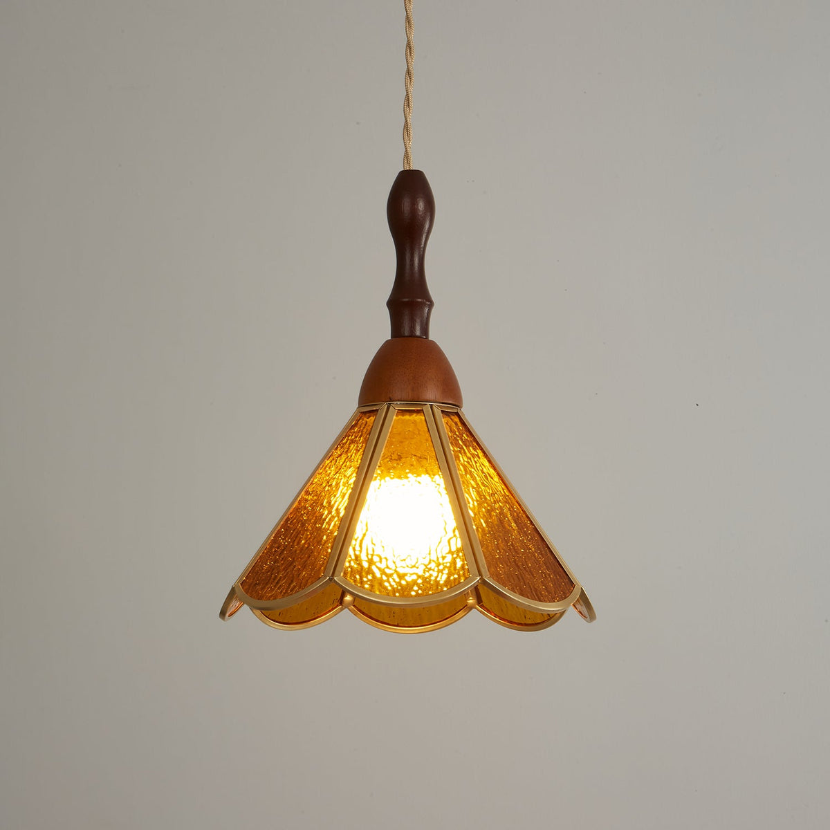 Closer view of the lit amber Clérachic pendant, its deep gold glass petals bright against a grey backdrop.