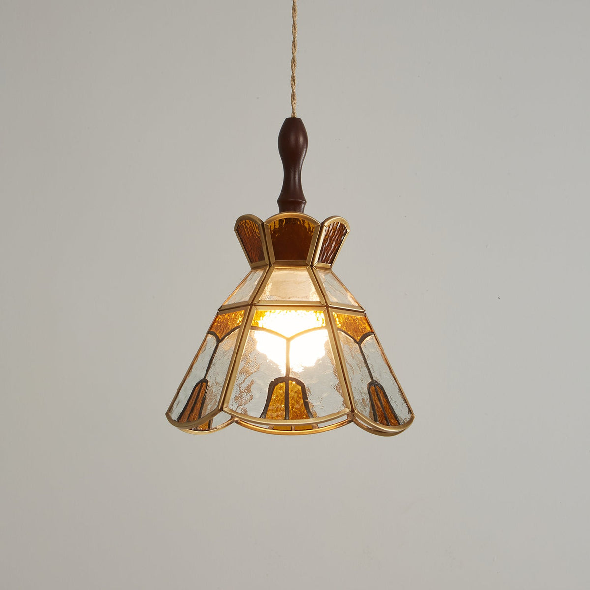Clérachic stained glass pendant with a stepped crown, glowing warm on a darker grey backdrop, with a wooden finial above.