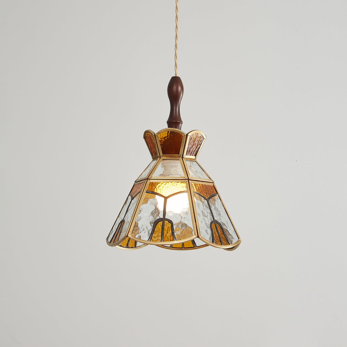 Clérachic pendant with clear and amber glass panels and a stepped crown, its bulb glowing behind rippled glass.