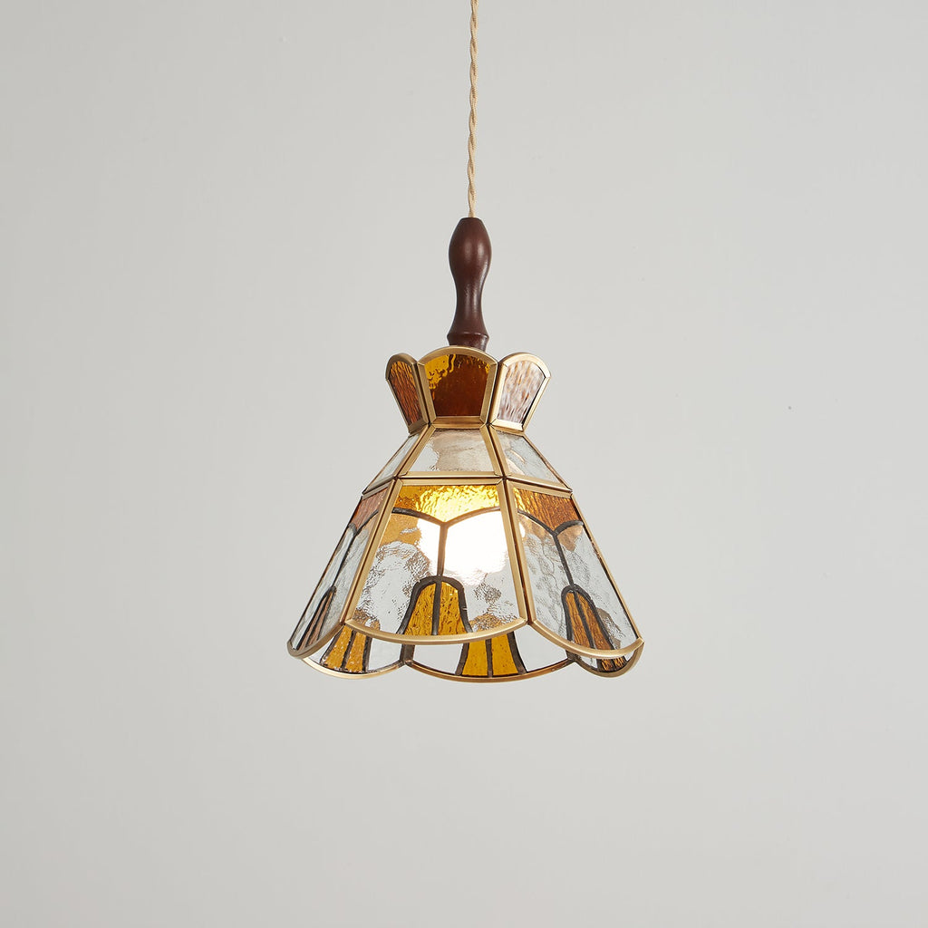 Lit Clérachic stained glass pendant with amber teardrop panels at the hem, shown on a grey backdrop.