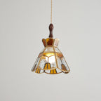 Lit Clérachic stained glass pendant with amber teardrop panels at the hem, shown on a grey backdrop.
