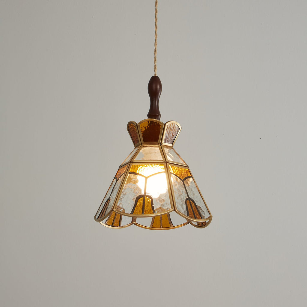 Clérachic stepped-crown pendant lit warm against a mid-grey backdrop, its amber and clear panels edged in brass.