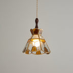 Clérachic stepped-crown pendant lit warm against a mid-grey backdrop, its amber and clear panels edged in brass.