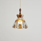 Clérachic stepped-crown pendant, slightly dimmer, its amber panels and brass edging clear against a pale grey wall.