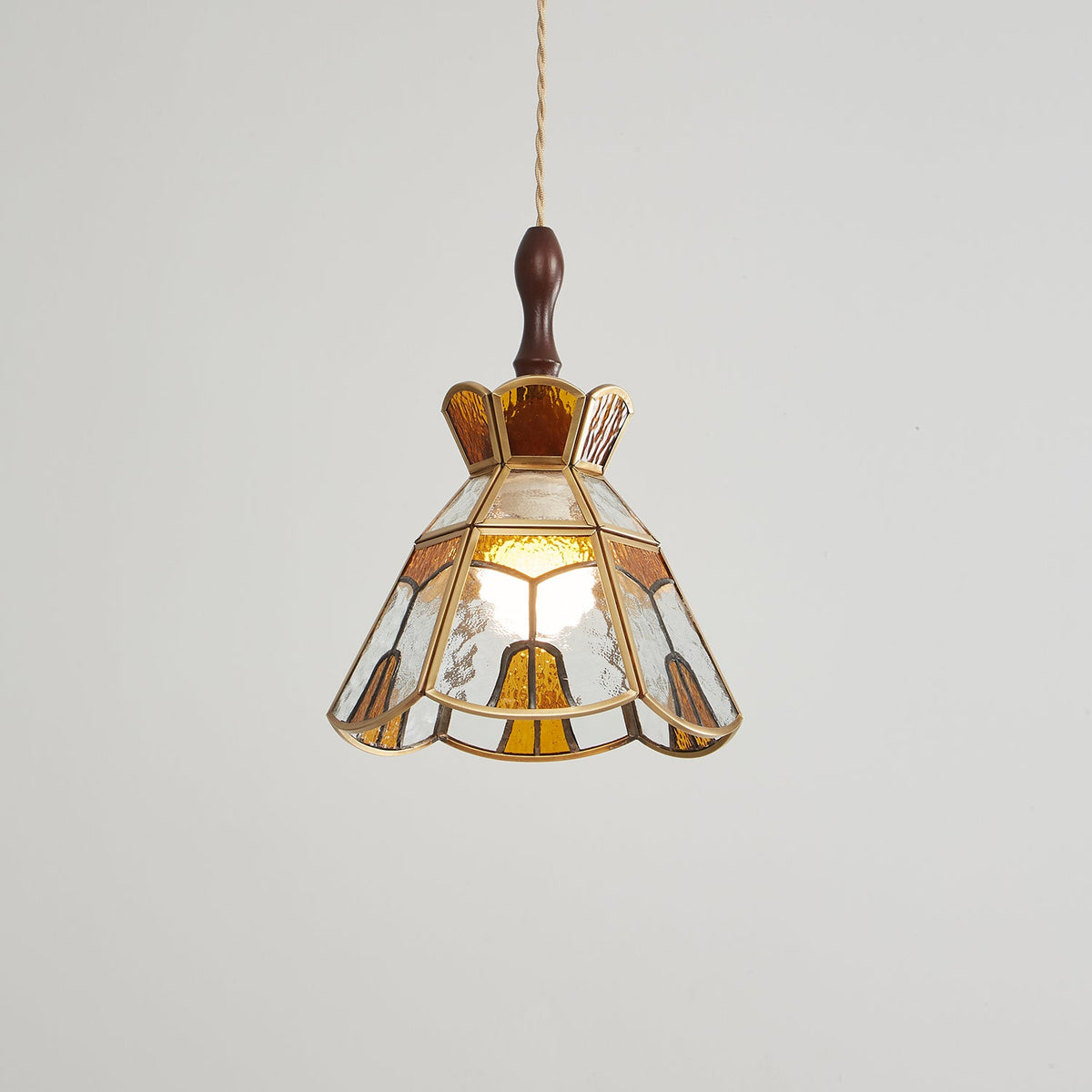 Clérachic stepped-crown pendant, slightly dimmer, its amber panels and brass edging clear against a pale grey wall.