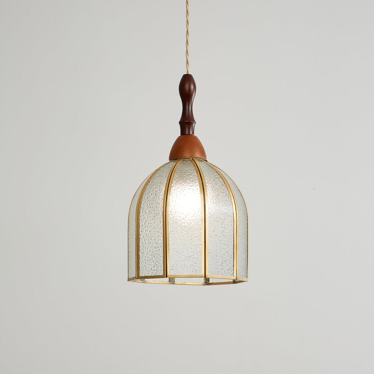 Faintly lit Clérachic domed pendant with textured clear glass between brass ribs, on a pale grey backdrop.