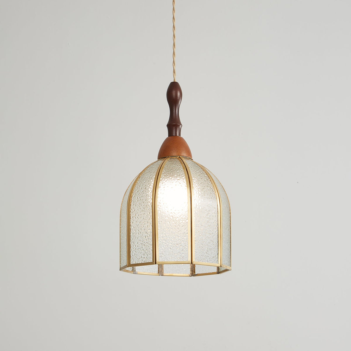 Clérachic domed pendant, lit, the bulb glowing through textured glass in an eight-rib brass frame.