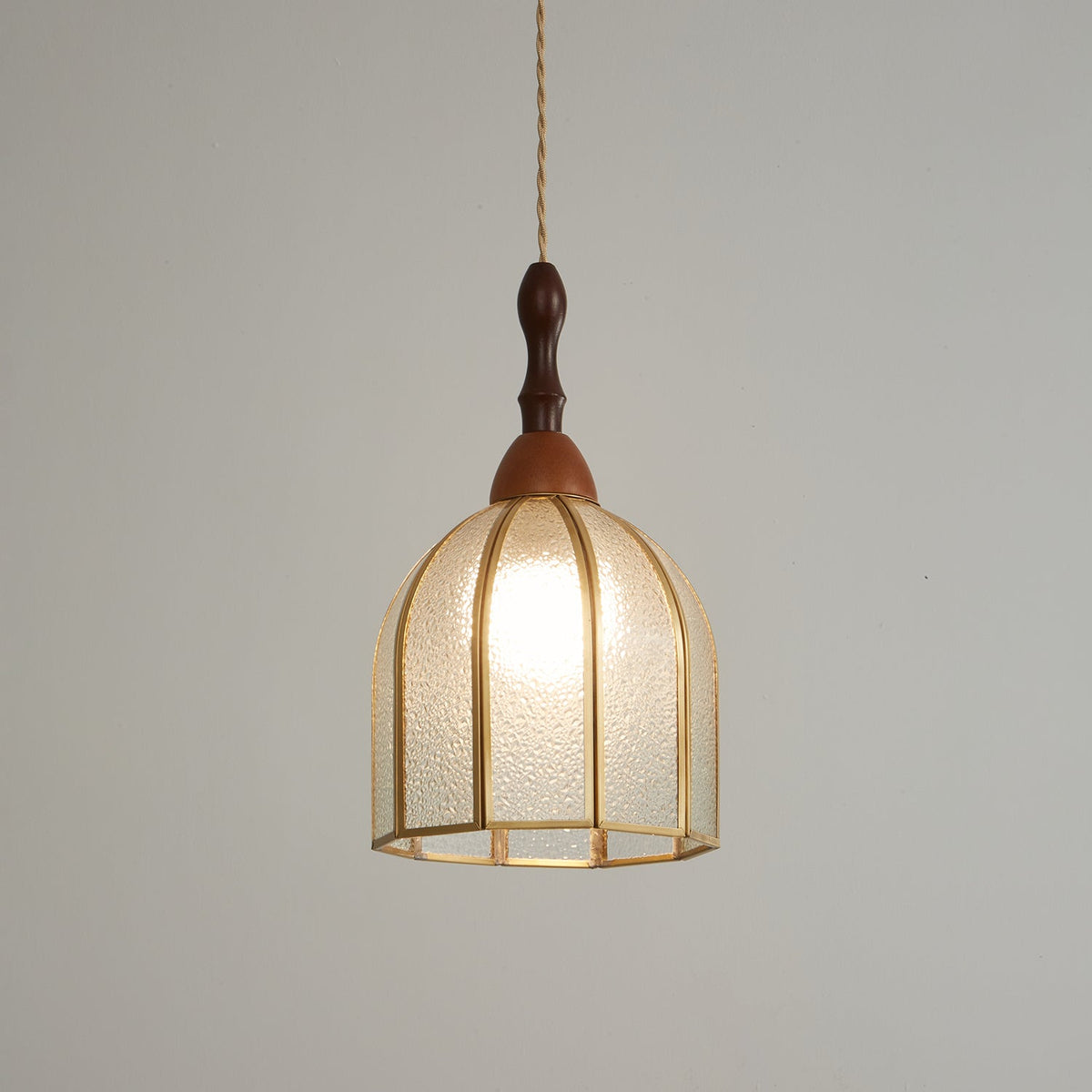 Clérachic domed pendant with brass ribs and rippled glass, the bulb glowing against a mid-grey backdrop.