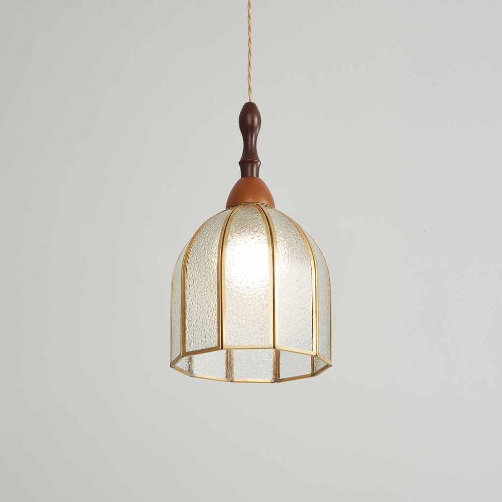 Clérachic domed pendant lit, its textured glass and open brass base catching the light on a pale backdrop.