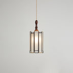 Lit Clérachic pendant with a tall frosted shade, the bulb glowing evenly behind panels in a dark metal frame.
