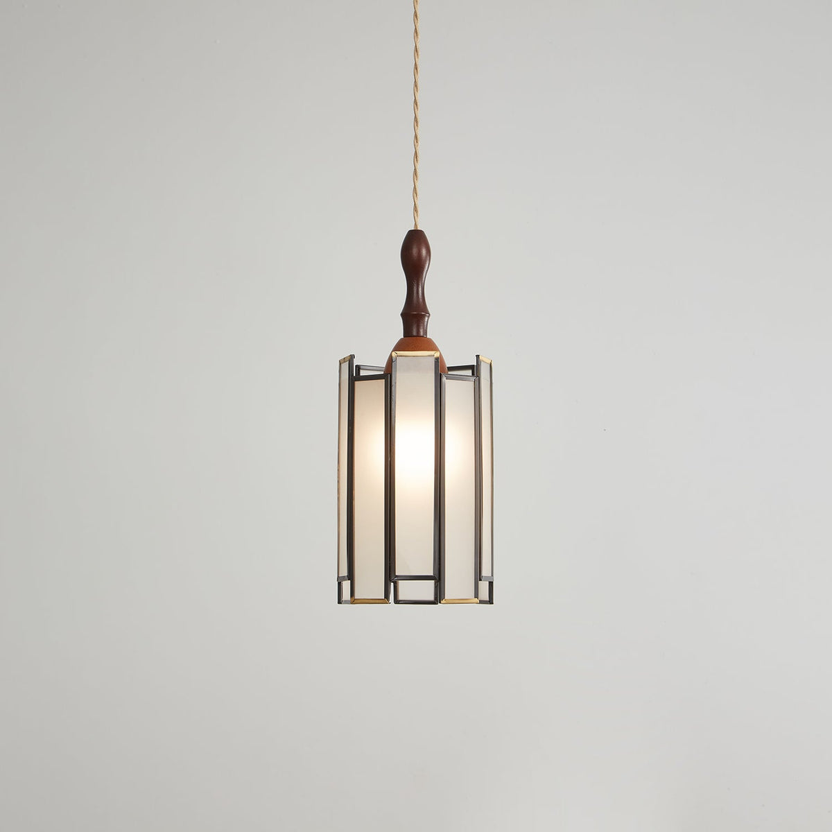 Lit Clérachic pendant with a tall frosted shade, the bulb glowing evenly behind panels in a dark metal frame.
