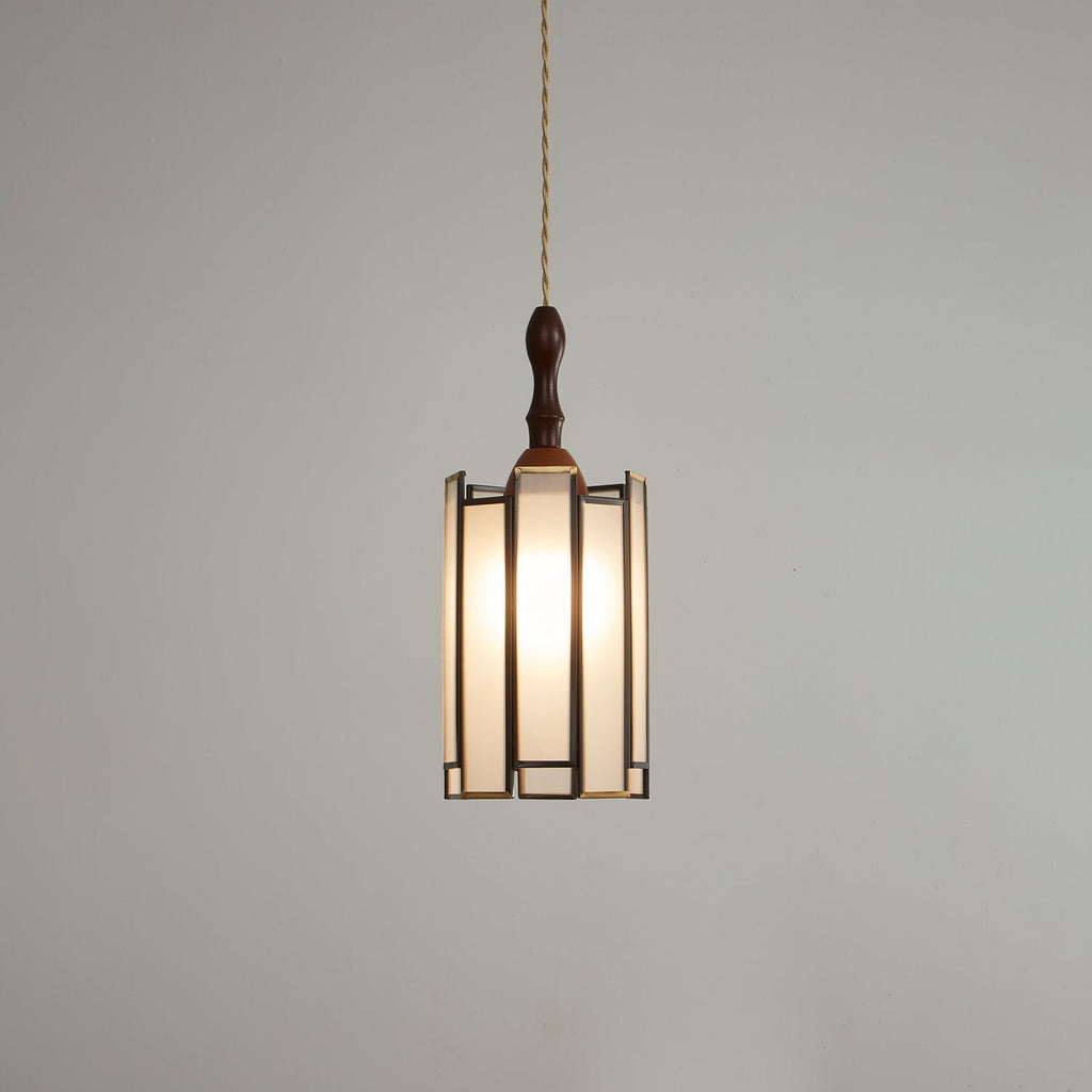 Lit Clérachic frosted-panel pendant on a darker grey backdrop, its dark frame with brass edges and a wooden finial above.