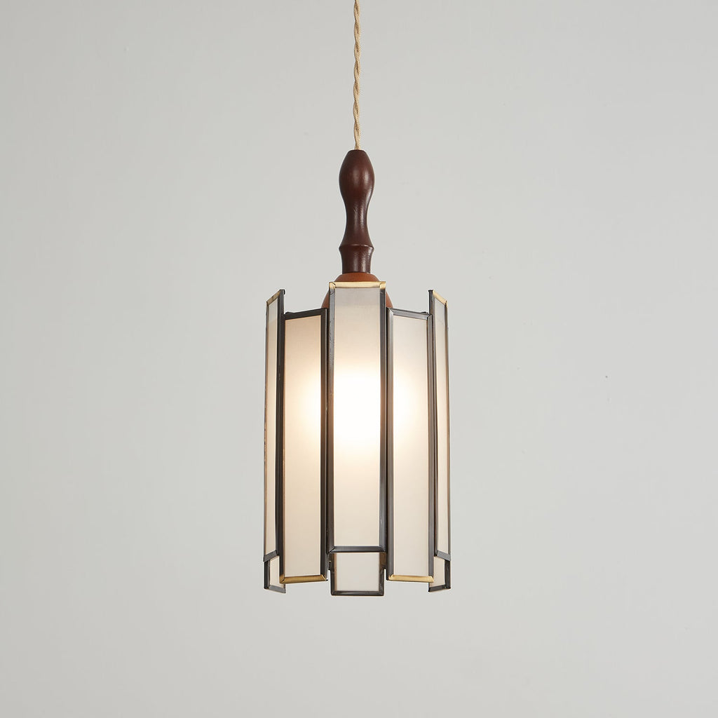 Larger Clérachic frosted-panel pendant, lit, with its dark frame, brass trim and glowing panels on a pale backdrop.