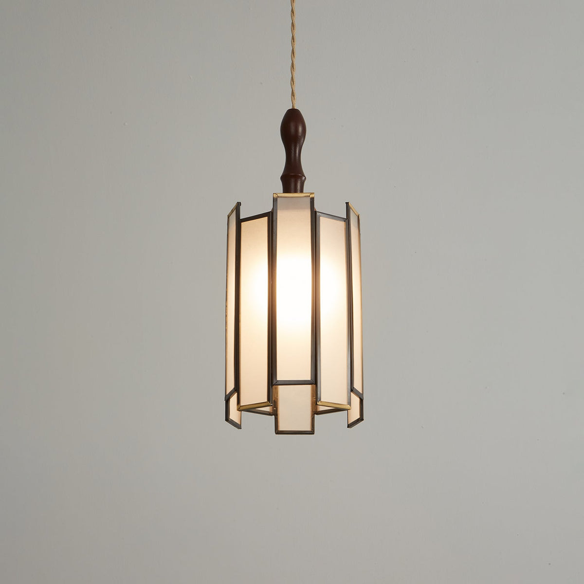 Clérachic frosted-panel pendant lit on a darker grey backdrop, with a slim finial and brass-edged panels.