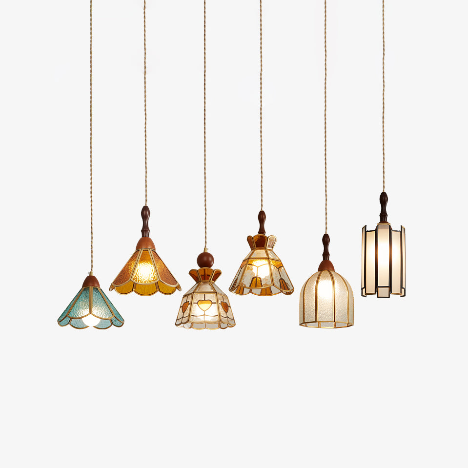 Six Clérachic stained glass pendant shapes hanging at staggered heights on a pale backdrop, each lit from within.